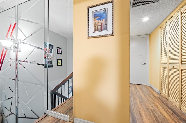 hall featuring visible vents, a textured ceiling, baseboards, and wood finished floors