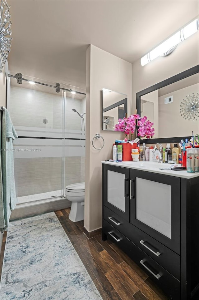 bathroom featuring visible vents, toilet, wood tiled floor, a shower stall, and vanity