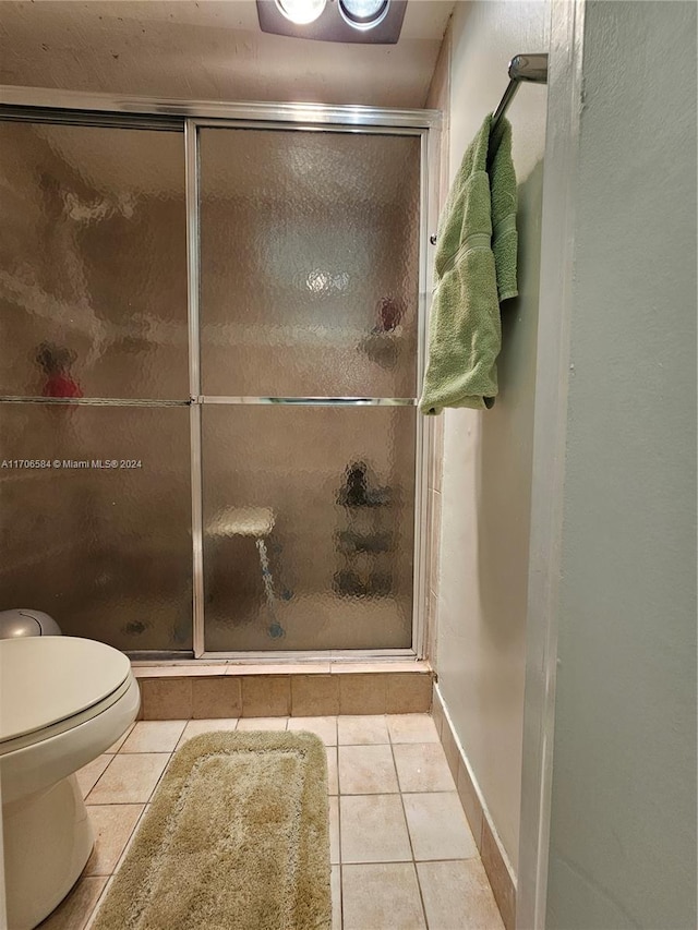 bathroom featuring tile patterned floors, toilet, and a shower with door