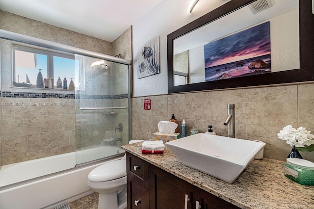 full bathroom featuring shower / bath combination with glass door, vanity, toilet, and tile walls