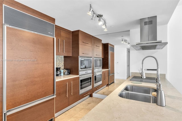 kitchen with built in appliances, light tile patterned flooring, wall chimney range hood, and sink