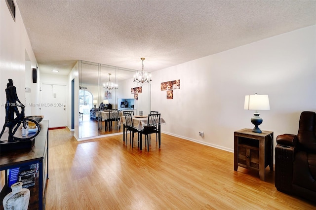 dining room with a notable chandelier, light wood-type flooring, and a textured ceiling