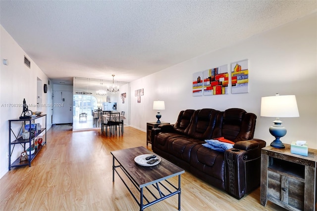 living room with a textured ceiling, a notable chandelier, and light wood-type flooring