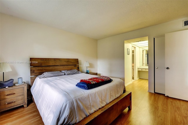 bedroom with ensuite bathroom, light wood-type flooring, and a textured ceiling