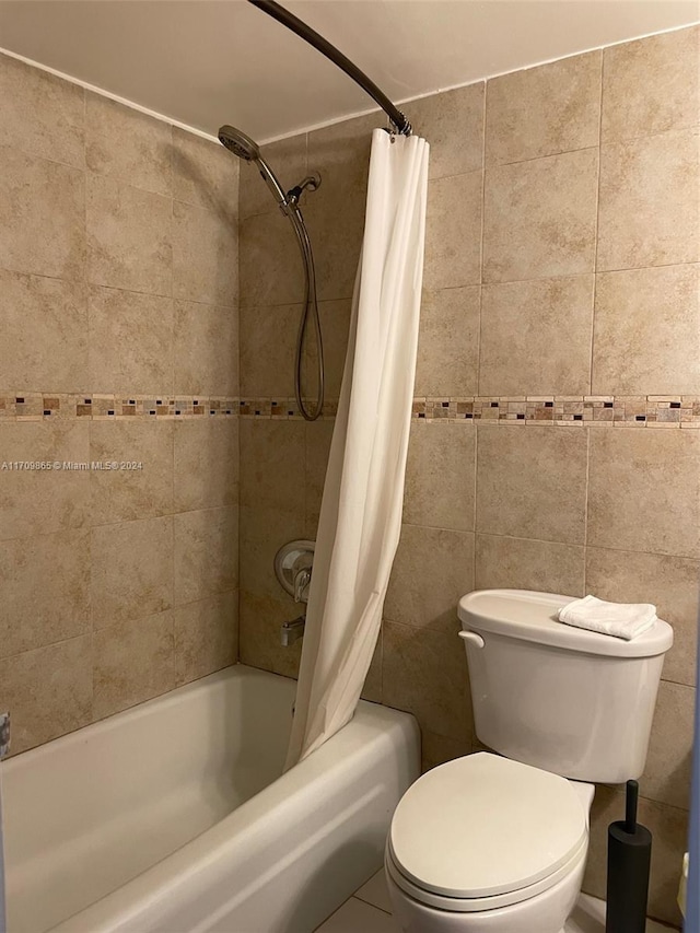 bathroom featuring tile patterned floors, toilet, shower / bath combo with shower curtain, and tile walls