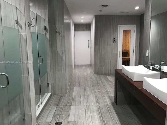 bathroom with vanity, a shower with door, and tile walls