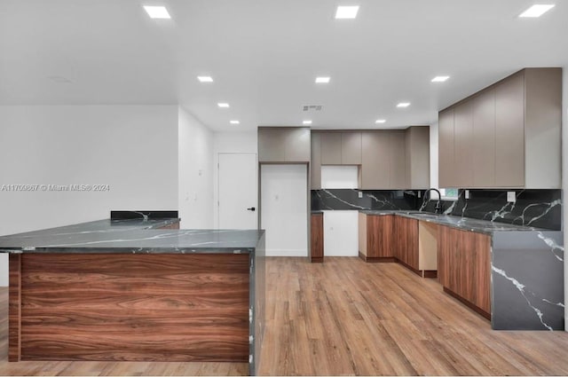 kitchen featuring dark stone countertops, kitchen peninsula, backsplash, and light hardwood / wood-style flooring