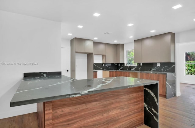 kitchen with dark stone counters, sink, light hardwood / wood-style flooring, tasteful backsplash, and kitchen peninsula