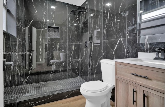 bathroom featuring hardwood / wood-style floors, vanity, toilet, tiled shower, and tile walls