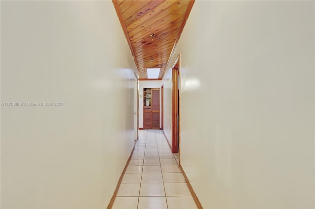 corridor with vaulted ceiling with skylight, light tile patterned floors, and wooden ceiling