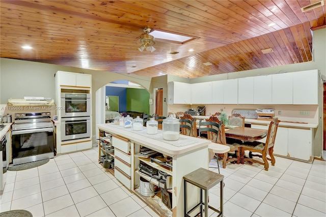 kitchen with wooden ceiling, stainless steel appliances, light tile patterned floors, vaulted ceiling with skylight, and white cabinets