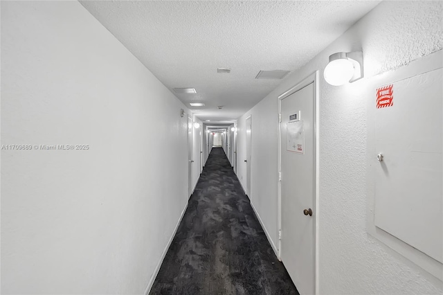 corridor with dark colored carpet and a textured ceiling