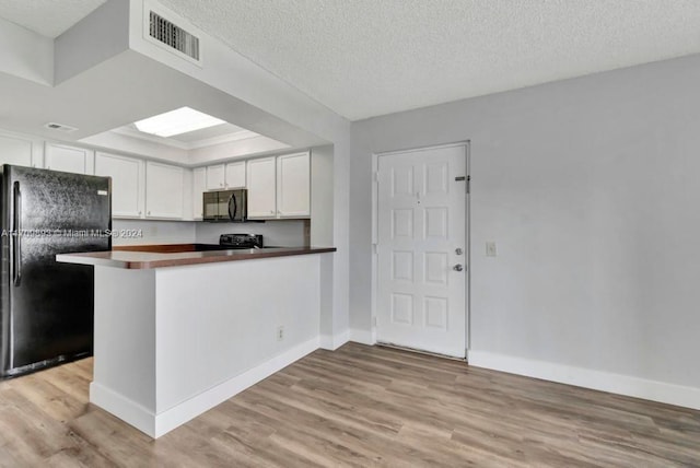 kitchen with kitchen peninsula, light wood-type flooring, a textured ceiling, black appliances, and white cabinetry