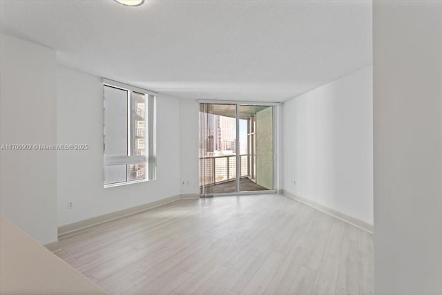 unfurnished room featuring floor to ceiling windows, light wood-type flooring, and a textured ceiling