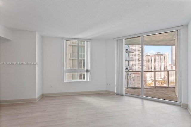 spare room with a textured ceiling, light hardwood / wood-style flooring, and expansive windows