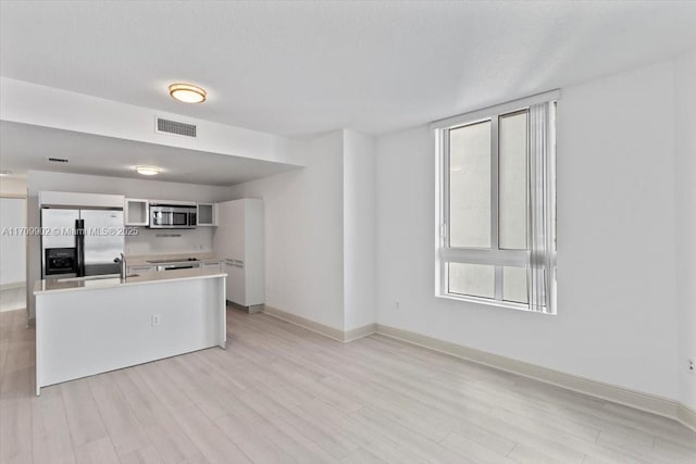 kitchen with white cabinetry, a center island with sink, stainless steel appliances, and light wood-type flooring