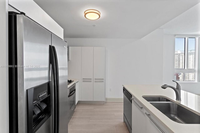 kitchen featuring white cabinets, light wood-type flooring, stainless steel appliances, and sink