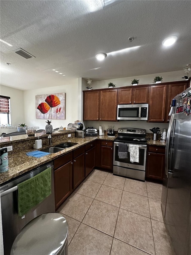 kitchen featuring a textured ceiling, sink, stainless steel appliances, and dark stone counters