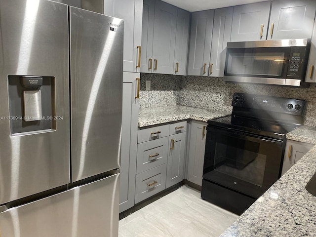 kitchen featuring backsplash, gray cabinetry, light stone counters, and appliances with stainless steel finishes