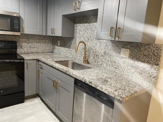 kitchen with gray cabinetry, light stone countertops, sink, stainless steel appliances, and decorative backsplash