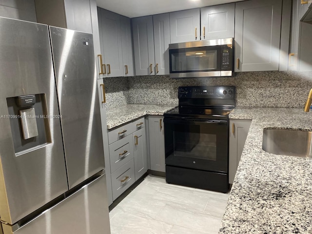 kitchen with gray cabinetry, sink, decorative backsplash, light stone countertops, and appliances with stainless steel finishes