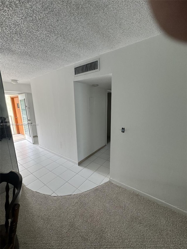 spare room with light colored carpet, visible vents, a textured ceiling, and light tile patterned flooring