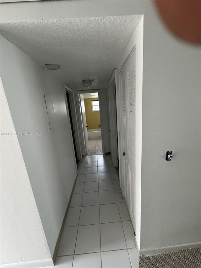 corridor featuring light tile patterned floors, baseboards, and a textured ceiling