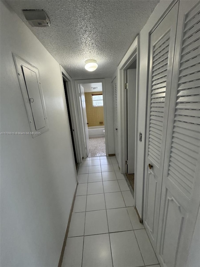 hallway featuring baseboards, visible vents, a textured ceiling, and light tile patterned flooring