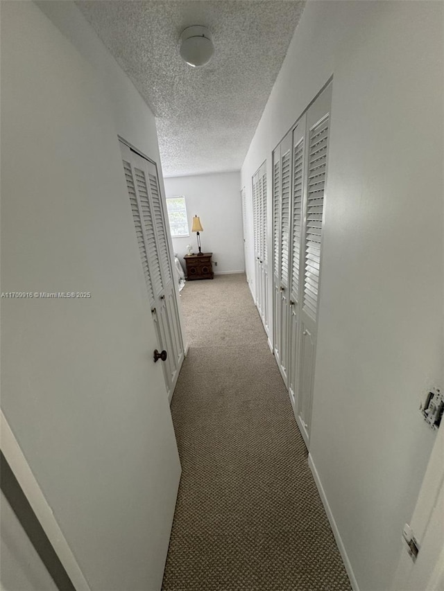 corridor with carpet, a textured ceiling, and baseboards