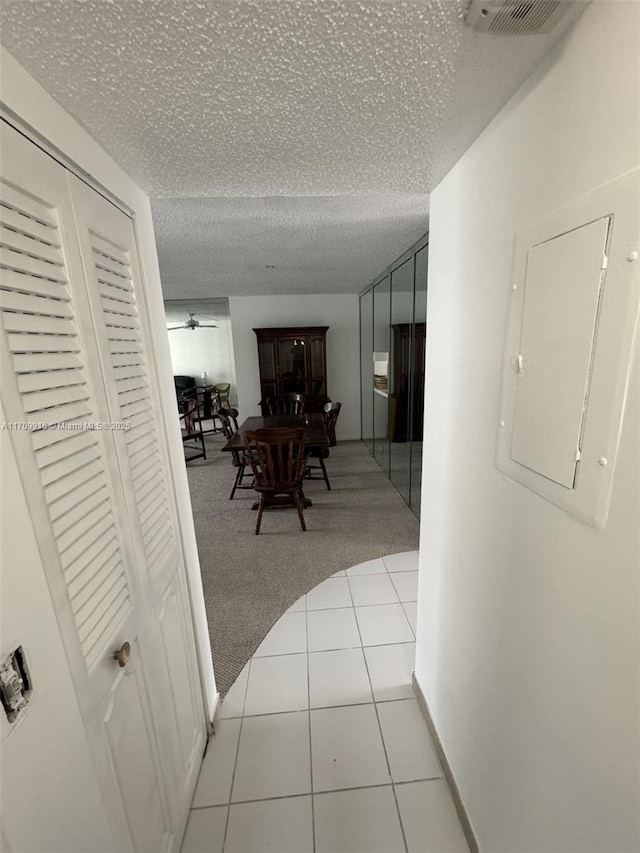 hall featuring light tile patterned floors, electric panel, visible vents, light colored carpet, and a textured ceiling