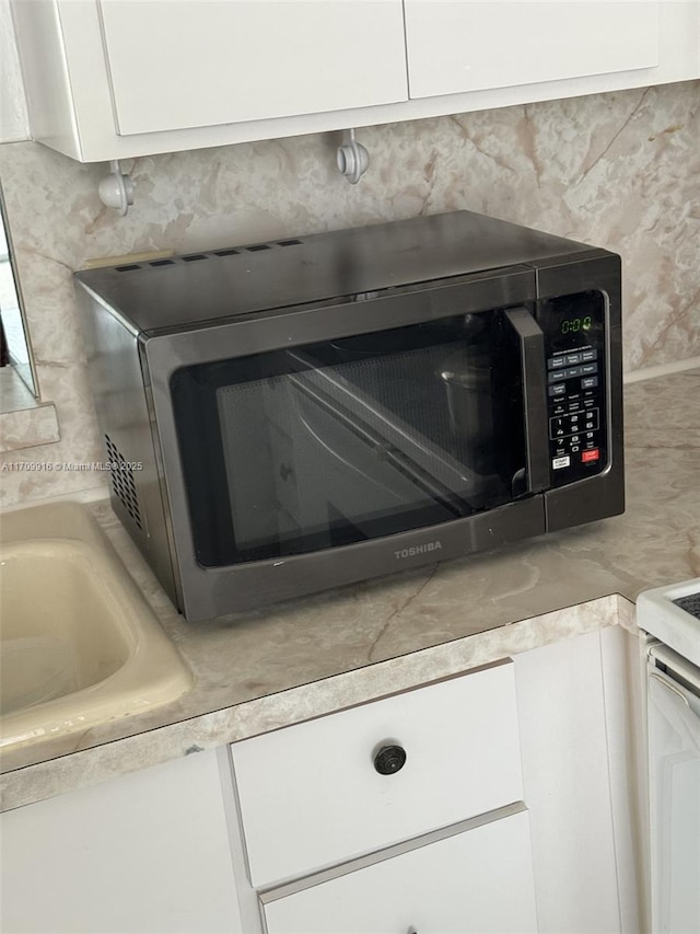 details with light countertops, stainless steel microwave, and white cabinetry