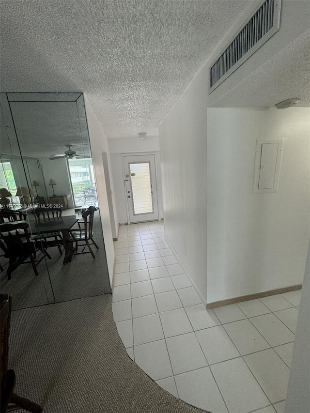 corridor with light tile patterned floors, a textured ceiling, and electric panel