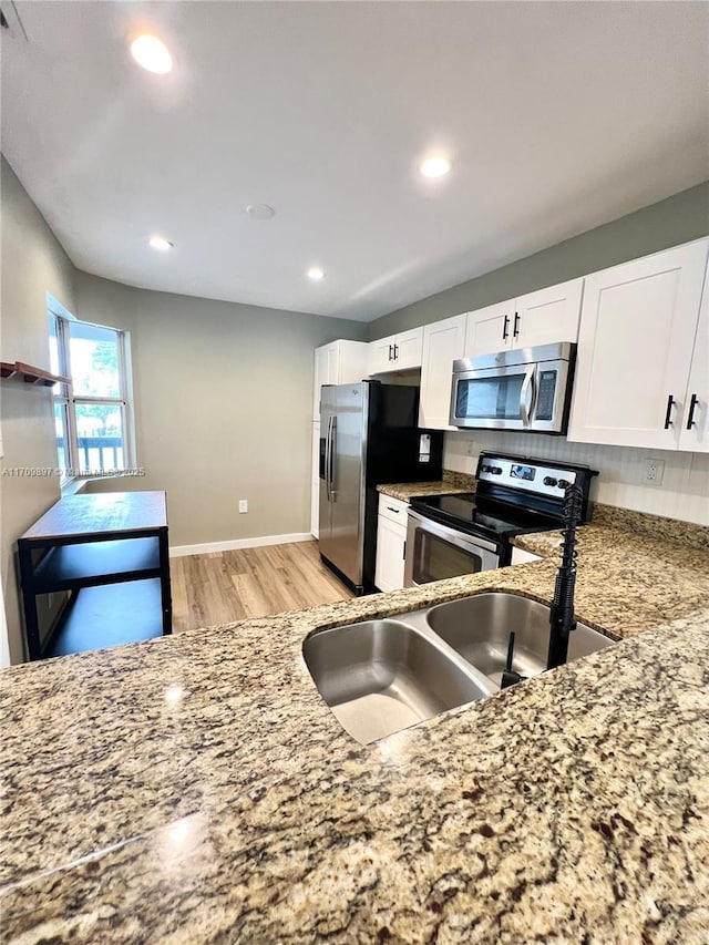 kitchen with white cabinetry, sink, light stone counters, stainless steel appliances, and light hardwood / wood-style flooring