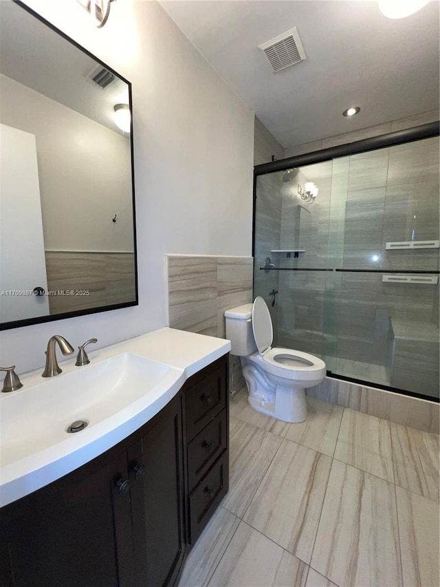 bathroom with vanity, toilet, a shower with door, and tile walls