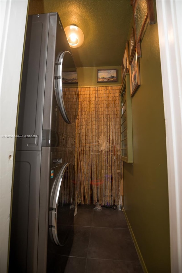 laundry room featuring stacked washer and clothes dryer, a textured ceiling, and dark tile patterned floors