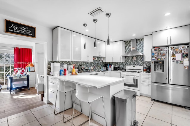 kitchen with white cabinetry, wall chimney range hood, stainless steel fridge with ice dispenser, white range with gas stovetop, and decorative light fixtures