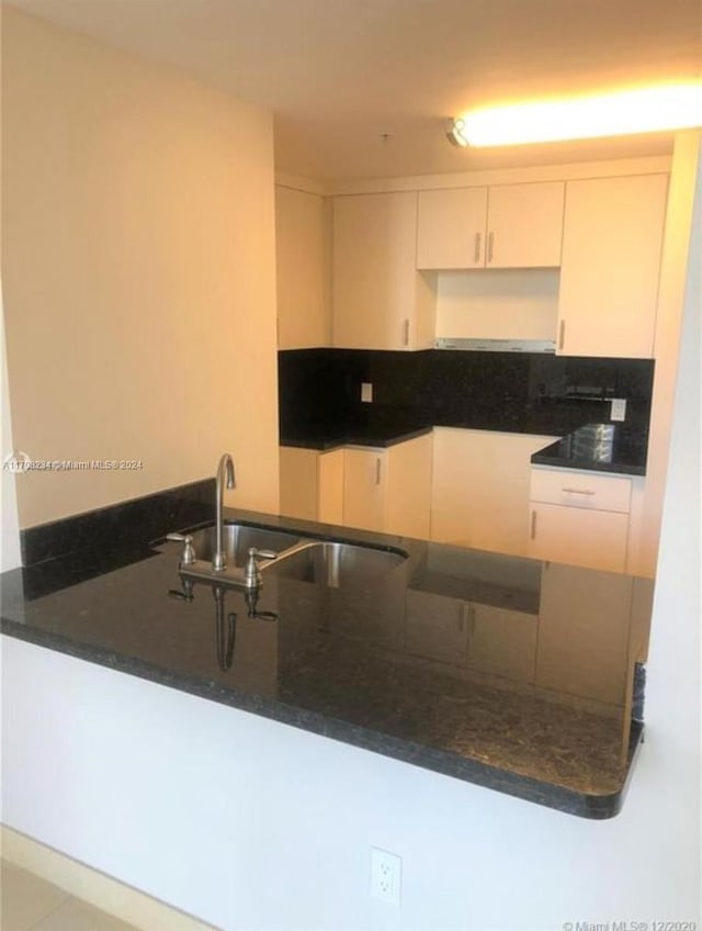 kitchen featuring white cabinets, kitchen peninsula, dark stone countertops, and sink