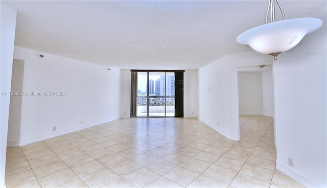 empty room with floor to ceiling windows, light tile patterned floors, and a textured ceiling