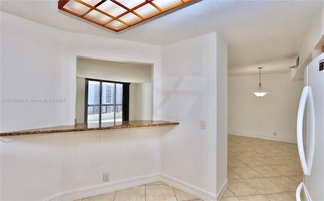 kitchen with stone counters, white fridge, a textured ceiling, decorative light fixtures, and light tile patterned floors