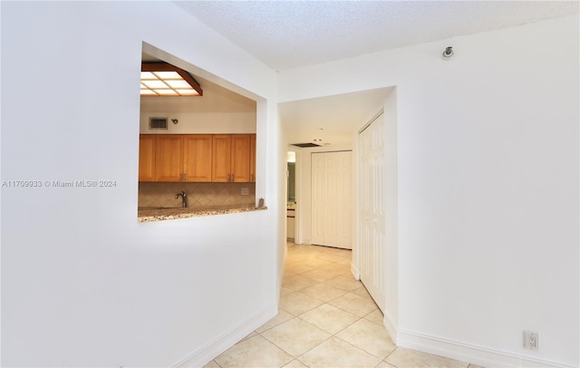 hall featuring sink, light tile patterned floors, and a textured ceiling