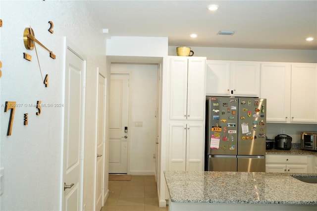 kitchen featuring white cabinetry, stainless steel fridge, light tile patterned floors, and light stone counters