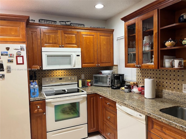 kitchen featuring backsplash, light stone counters, a textured ceiling, white appliances, and sink