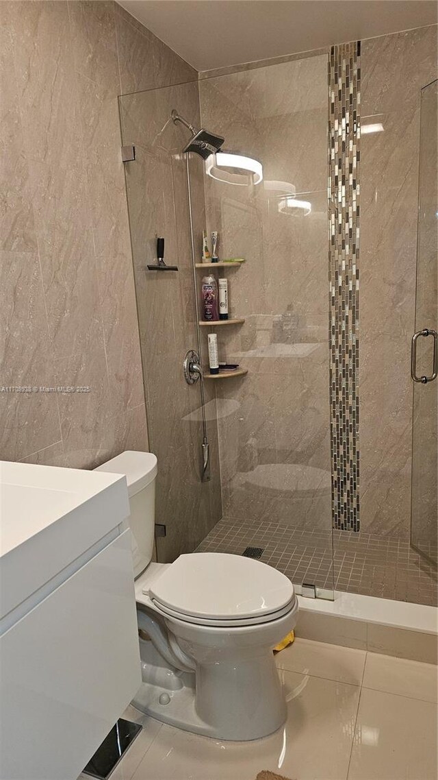 bathroom featuring tile patterned floors, an enclosed shower, toilet, vanity, and tile walls