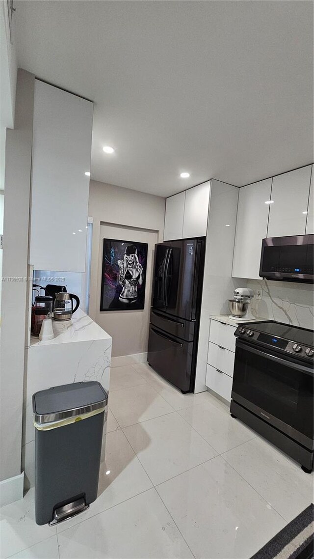 kitchen with black appliances, light tile patterned flooring, white cabinets, and tasteful backsplash