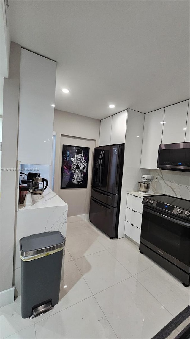 kitchen featuring range with electric stovetop, light countertops, stainless steel microwave, freestanding refrigerator, and white cabinets