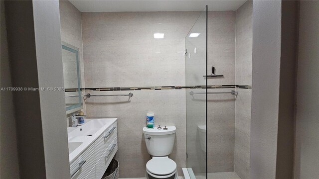 bathroom with tiled shower, vanity, tile walls, and toilet