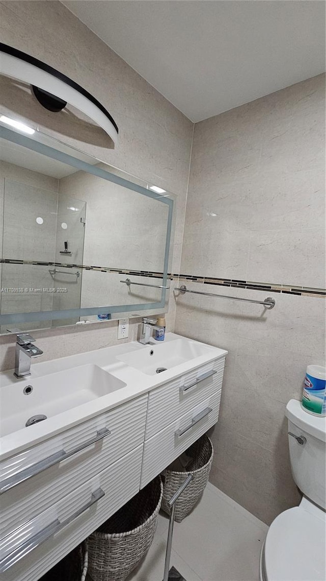 bathroom with toilet, double vanity, a sink, and tile walls