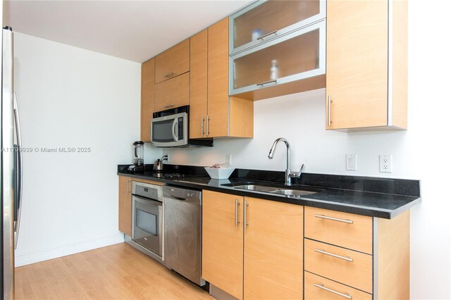 kitchen with sink, stainless steel appliances, light hardwood / wood-style floors, and dark stone countertops