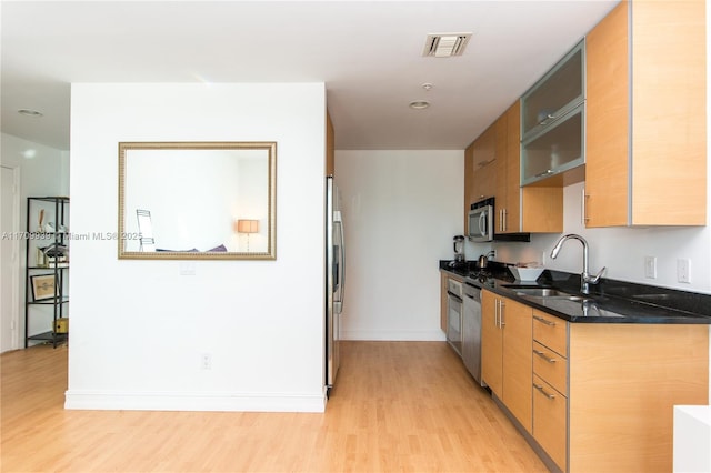 kitchen featuring stainless steel appliances, dark stone countertops, light hardwood / wood-style flooring, and sink