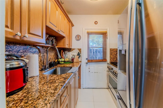 kitchen with dark stone countertops, sink, light tile patterned floors, and appliances with stainless steel finishes